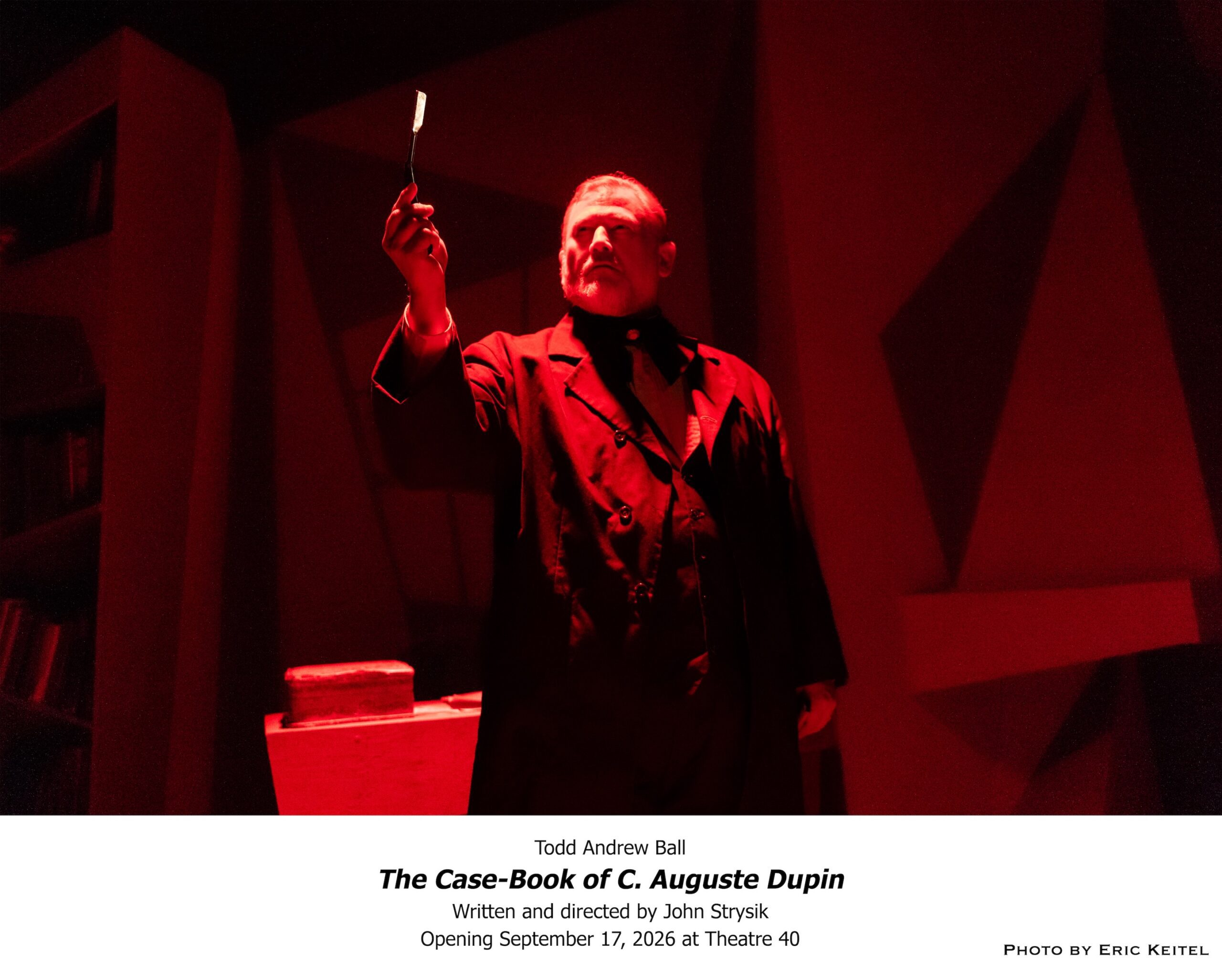 : Todd Andrew Ball examines a piece of evidence under dramatic red lighting in Theatre 40’s The Case-Book of C. Auguste Dupin. Photo by Eric Keitel.